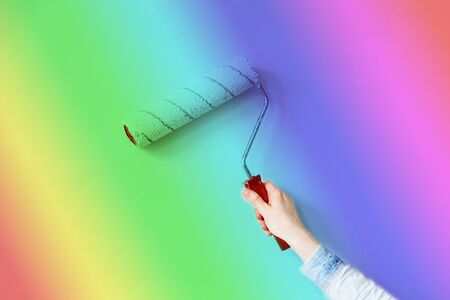The LGBT community. Human hand painting wall in rainbow colors as LGBTQ community symbol. Close up of Decorator's hand painting wall with roller. Copy spaceの写真素材