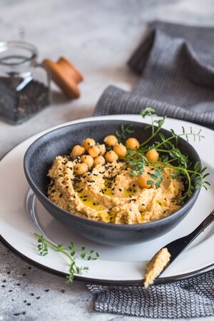 Chickpeas hummus in the black bowl decorated with sesame seeds and chickpeas greens. Vegan recipes, plant-based dishes. Green living concept. Organic food. Vegetarian cuisine.の写真素材