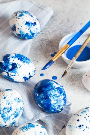 Dyed Easter eggs. Ð¡lassic blue 2020 Easter eggs on the grey background. Blue speckled easter eggs with paint and brushes. Decorating eggs, preparing for Easterの写真素材