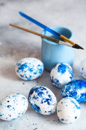 Dyed Easter eggs. Ð¡lassic blue 2020 Easter eggs on the grey background. Blue speckled easter eggs with paint and brushes. Decorating eggs, preparing for Easterの写真素材