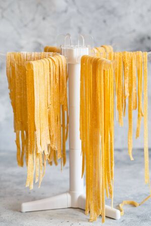 Homemade Italian tagliatelle hanging on a pasta drying rack. Fresh noodle drying on drying rack.  Self-made Spaghetti Drying on a Pasta Rack. Homemade fresh egg pasta linguine hanging on rack to dryの写真素材