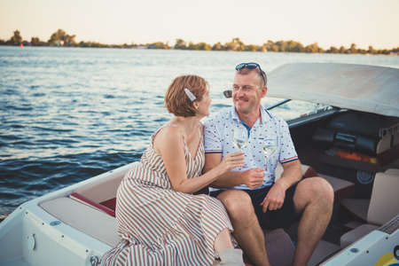Beautiful couple man and woman drink wine while sitting in a boat. Romantic relationship. Celebrating wedding anniversary.の写真素材
