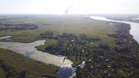 Drone fly over waving river surrounded by local village. Fire in reed marshes aerial view. Top view.の写真素材