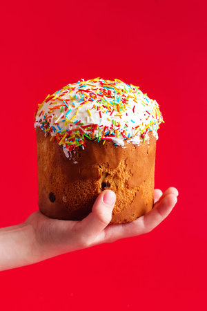 Children's hand holds Easter Cake in front of red background. Russian and Ukrainian Traditional...