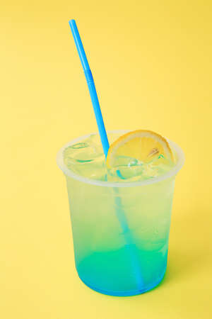 A glass with lemonade blue with lemon, cold refreshing drink or beverage with ice on yellow backgroundの写真素材