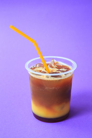 A glass with orange coffee cocktail, cold refreshing drink or beverage with ice on violet backgroundの写真素材