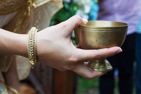 Bride hand holding gold container for pour water ceremonyの写真素材