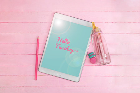 Pink wording Hello Tuesday on screen tablet with pink wood background