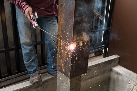 Worker welding steel with spark lighting and smoke at construction site