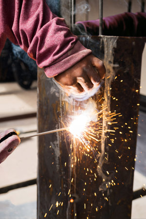 Worker welding steel with spark lighting and smoke at construction site