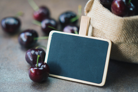 Fresh organic cherries in burlap sack with blank blackboardの写真素材
