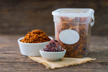 Spicy chili paste in white ceramic and plastic containers on wood background