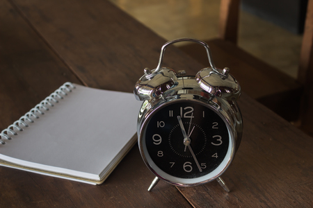 Retro alarm clock with blank realistic spiral notepad notebook on wooden table, stock photoの写真素材