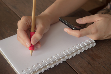 Hand of woman writing notebook and looking smartphone on wooden table, stock photoの写真素材