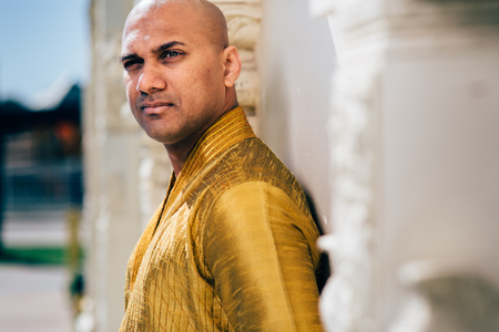 The handsome Indian man wears a gold kurta and posed at a temple.の写真素材