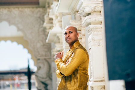 The handsome Indian man wears a gold kurta and posed at a temple.の写真素材