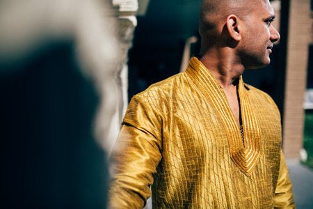 The handsome Indian man wears a gold kurta and posed at a temple.の写真素材