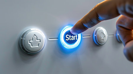 Close-up view of a person's finger pressing an illuminated start button on a modern control panel, symbolizing technology and machine activation.の素材