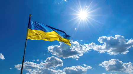A vibrant Ukrainian flag waves under a bright sun in a clear blue sky adorned with white clouds, symbolizing national pride and beauty in nature.の素材