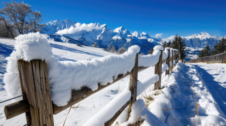 A stunning winter landscape featuring a snow-covered fence with majestic mountains in the background under a clear blue sky, evoking tranquility and beauty.の素材