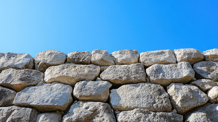 A sturdy stone wall is captured under a bright blue sky, showcasing the texture and structure of the stones in a serene outdoor setting.の素材