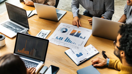 A diverse group of professionals collaborates in a modern office setting, analyzing data on laptops and discussing insights from charts and reports.の素材