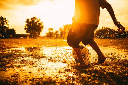 An action sport picture of a group of kids playing soccer football for exercise in community rural area under the sunset.の写真素材