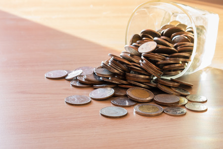 Coins in money jar with sunset light in saving money concept on wooden backgroundの写真素材