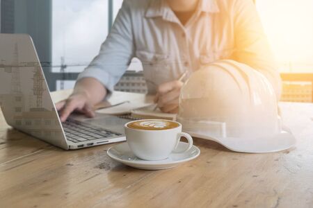 double exposure of engineering useing laptop computer on wooden table and working site with a cup of coffee at site office.の写真素材