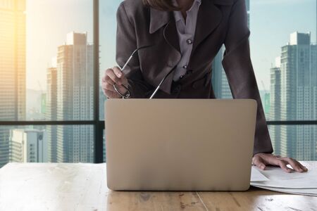 Business woman standing hand holding glasses and document finacial report wokring with laptop computer. selective focus on glasses.の写真素材