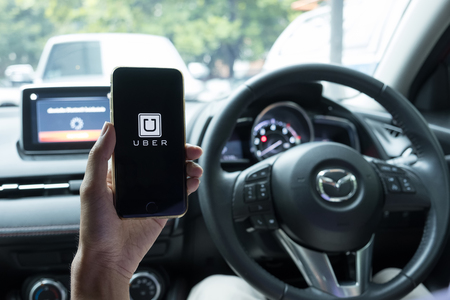 CHIANG MAI,THAILAND - JUNE 15, 2017 : A man hand holding Uber app showing on iPhone 6s on road and black car, Uber is smartphone app-based transportation network.のeditorial素材