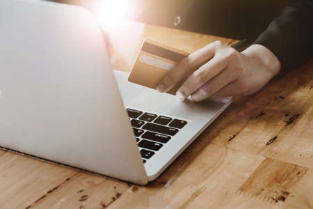 Close up hand of woman holding credit card and using laptop computer. Online shopping concept with vintage filter toneの写真素材