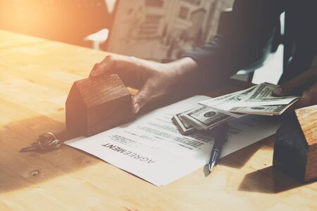 Real estate agent with house model and bank notes in hands putting signing contract. Buy - sell house.の写真素材