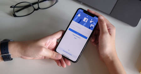 CHIANG MAI ,THAILAND - JULY 3, 2020 : Woman hand holding iPhone X to use facebook with new login screen.Facebook is a largest social network and most popular social networking site in the worldのeditorial素材