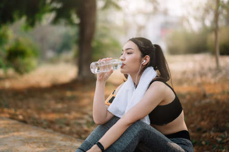 Young woman athlete takes a break, drinking water, out on a run on a hot day.の写真素材