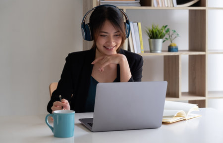 Happy asian woman wear headset laugh using laptop video stream conference call teach online, happy ethnic girl student gamer tutor have fun watch webinar web cam education entertainment conceptの写真素材
