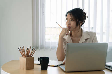 Portrait of business asian woman thinking and working with laptop computer in officeの写真素材