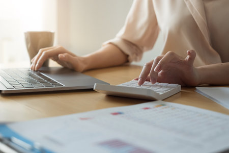 Close up hand of woman using computer calculating household finances or taxes on machine, female manage home family expenditures, using calculator, make payment on laptopの写真素材
