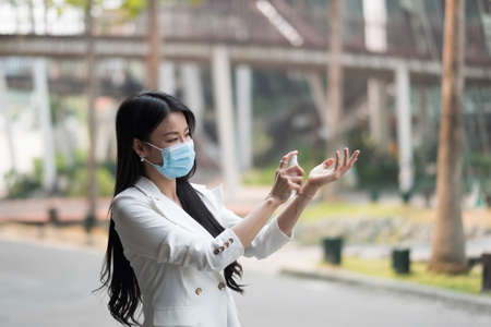 Portrait of businesswoman wearing mask sanitizing hands at post pandemic office, copy space.の写真素材