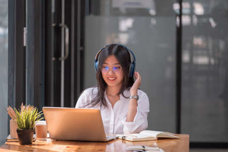 Asian girl with glasses look at laptop while doing homework making video call abroad using internet friend connection, Online learning education concept.の写真素材