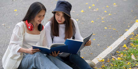 Two happy students sitting and talking each other in a campus at the park.の写真素材