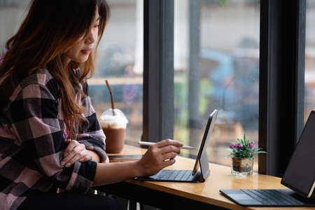 Young creative designer holding stylus pen drawing on screen of digital tablet at cafeの写真素材