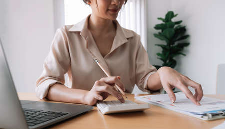 Close up of businesswoman or accountant hand holding pencil working on calculator to calculate financial data report, accountancy document and laptop computer at office, business concept.の写真素材