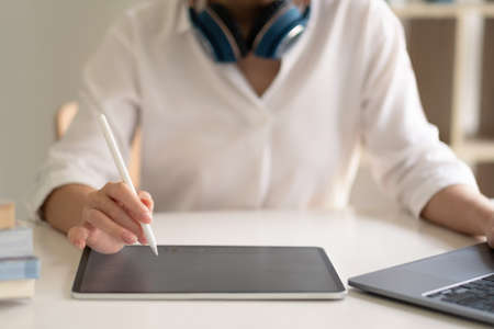Close up of female worker working from home with digital tablet, laptop and headphone in home office room.の写真素材