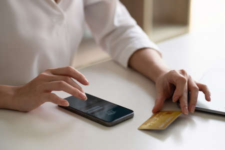 Close up woman using smart phone and laptop computer and credit card for shopping online at home.の写真素材