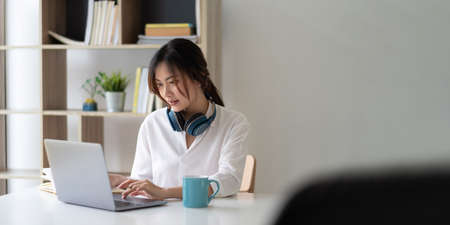 Portrait of a pretty young asian woman studying online with laptop computer while sitting at the...