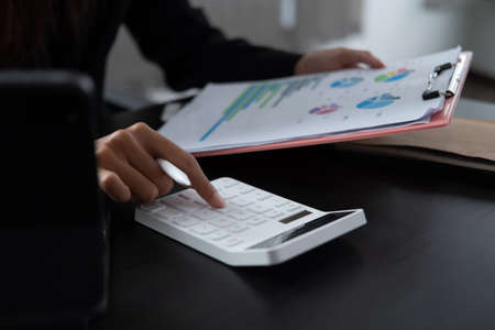 Woman with financial report and calculator. Woman using calculator to calculate report at the table in officeの写真素材