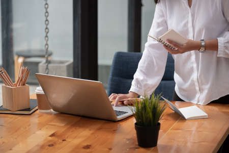 Cropped photo of woman writing making list taking notes in notepad working or learning on laptop indoors- educational course or training, seminar, education online concept.の写真素材