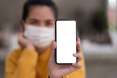 Mockup image of a beautiful woman wear mask while holding mobile phone with blank white screen.の写真素材