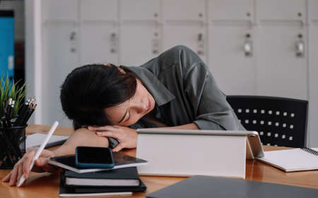Overworked tired businesswoman sleeping on table in office. Young exhausted girl working from home. Woman using laptop. Entrepreneur, business, freelance work, student, stress, work from home concept.の写真素材
